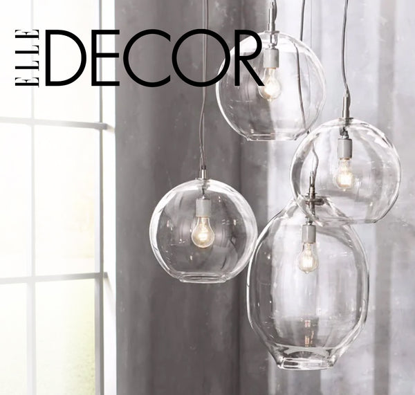 Elle Decor feature: Cluster of four Simon Pearce Woodstock and Essex glass globe pendant lights with Edison bulbs, hanging against a gray linen curtain