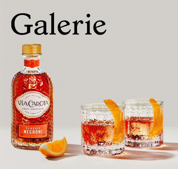 Galerie magazine feature: Simon Pearce Greenwich Lowball glasses filled with Negroni cocktails and garnished with orange twists, alongside a bottle of Via Carota Classic Negroni