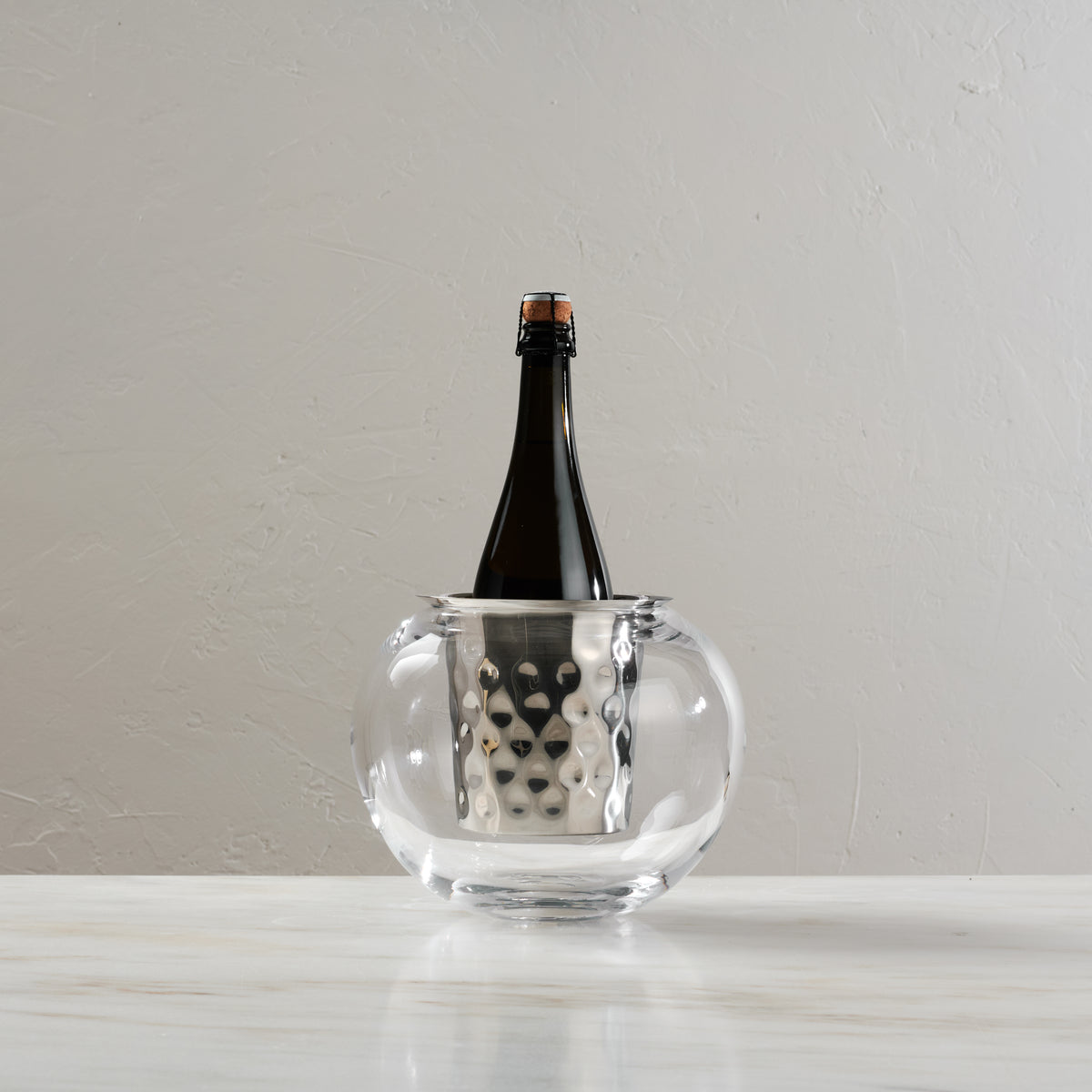 Clear glass wine chiller bucket with textured metal interior band holding a dark wine bottle.