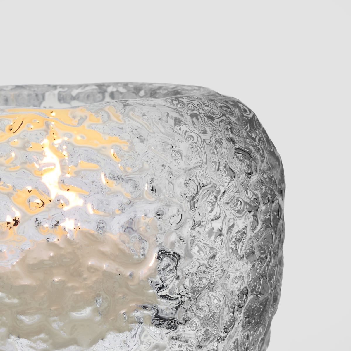 White textured tealight holder with lit yellow flame visible through cutout opening.