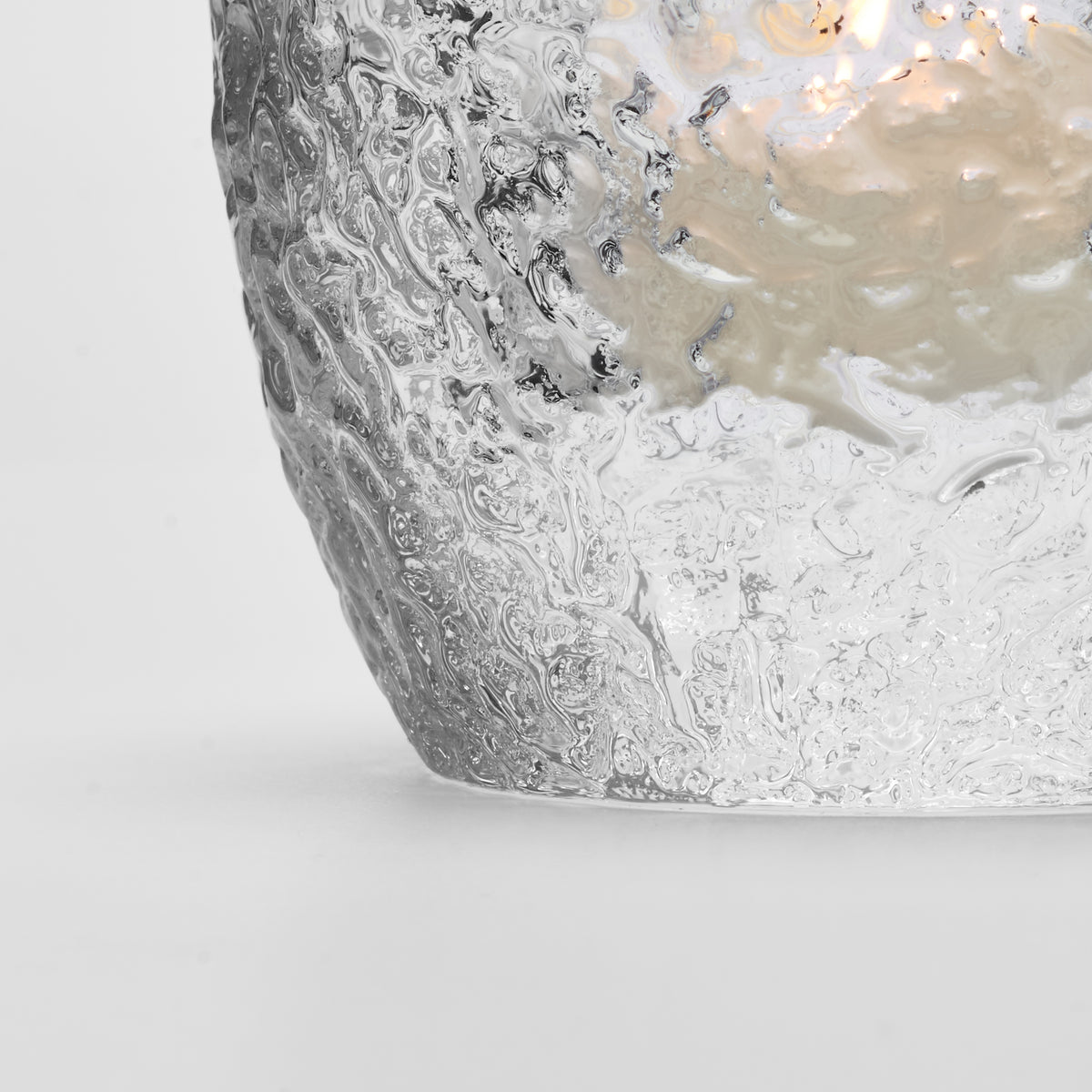 Clear glass tealight holder with textured snowball-like surface and lit candle inside.