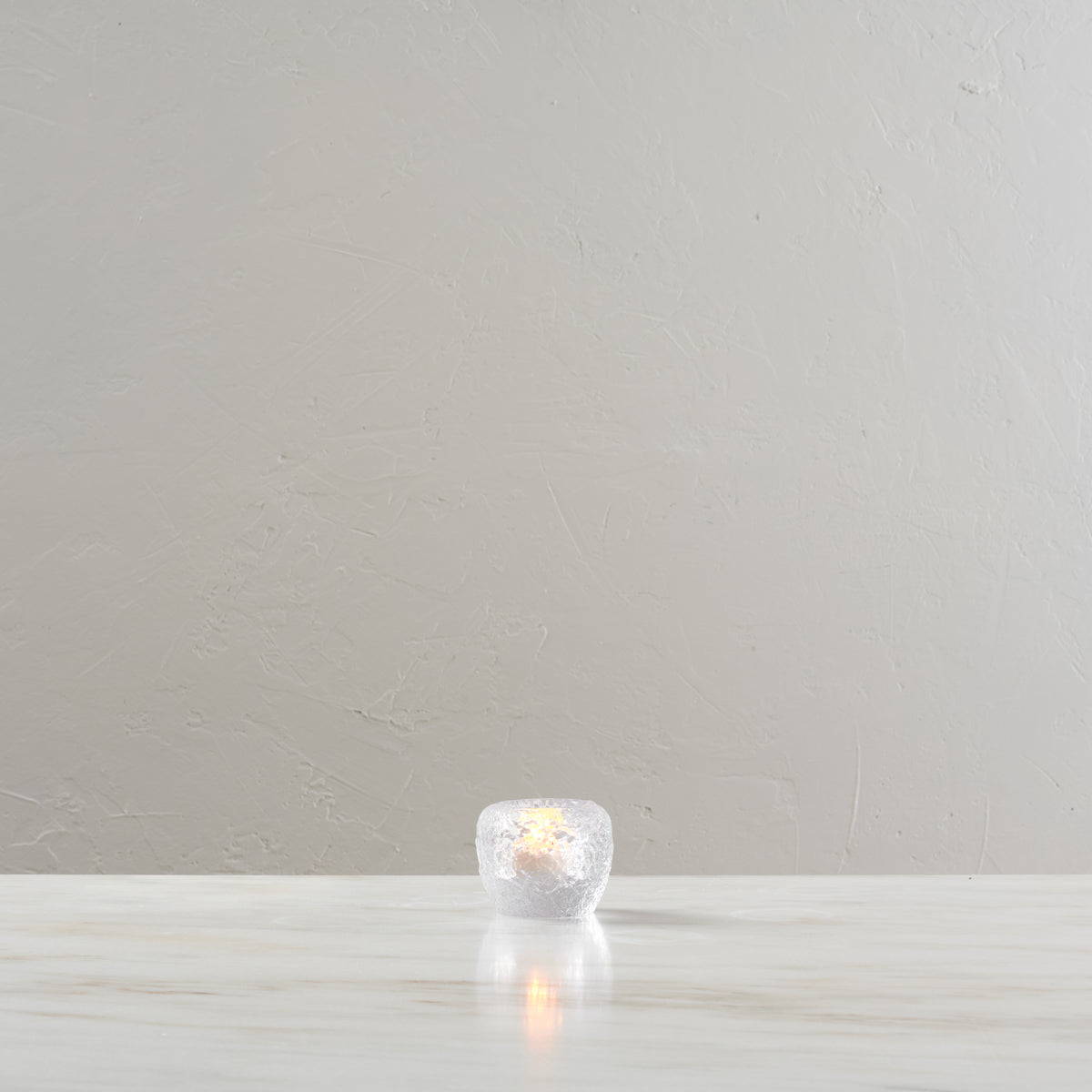 White spherical tealight holder with lit candle inside, displayed on light wooden surface.