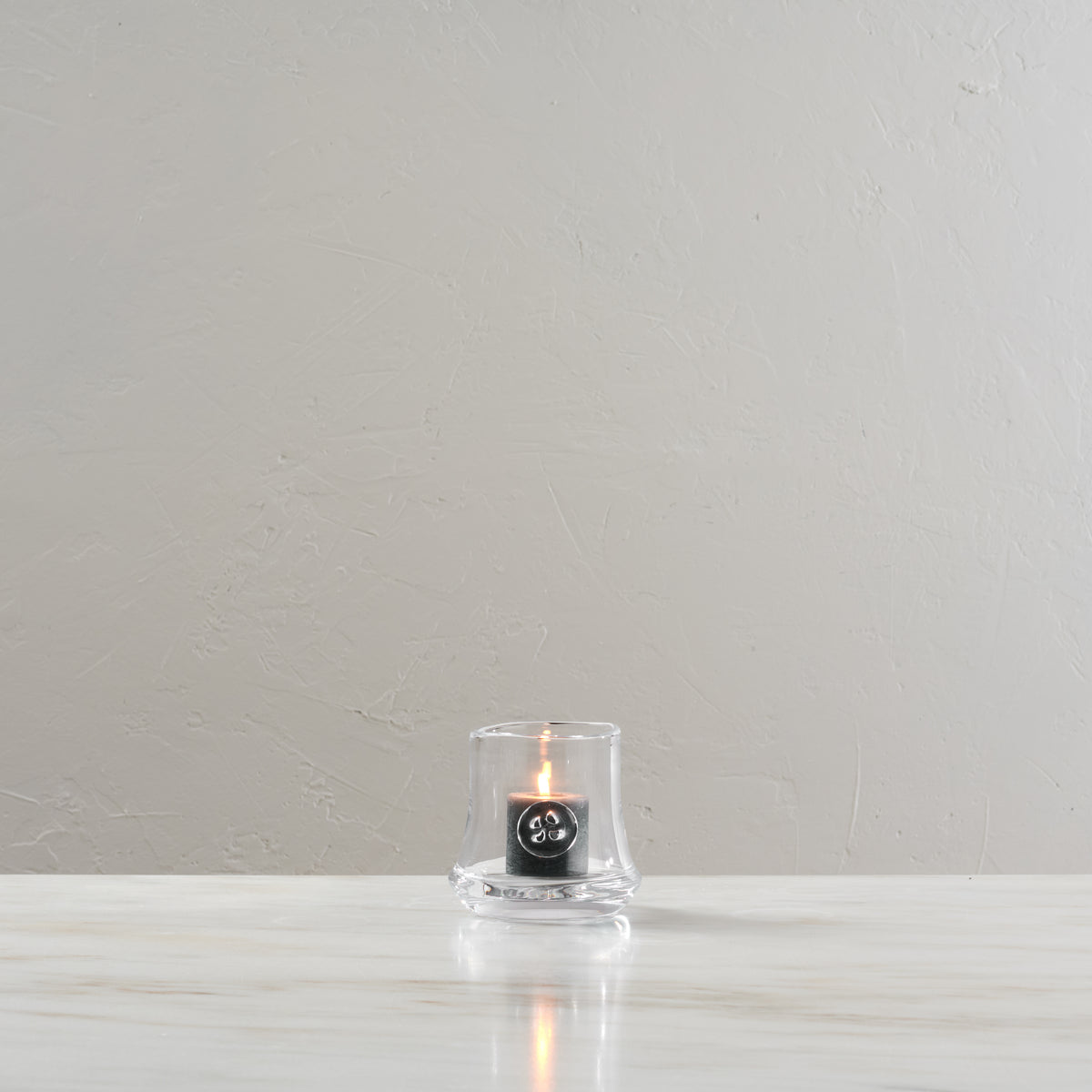 Small glass hurricane candle with black label and lit flame inside.