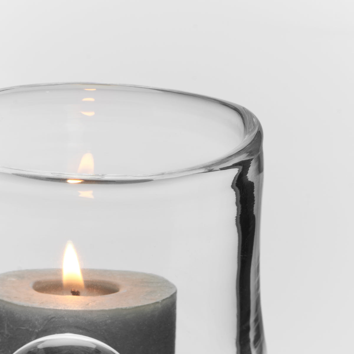 Clear glass hurricane with lit candle inside and black brushstroke detail on exterior.