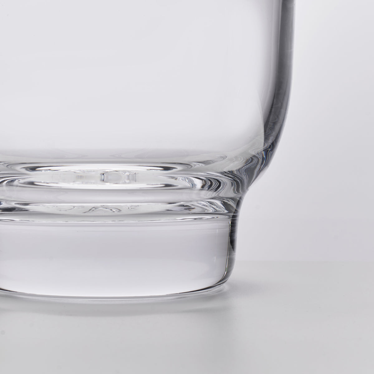 Clear glass ice bucket with cylindrical body and wide flat base, shown from side angle.