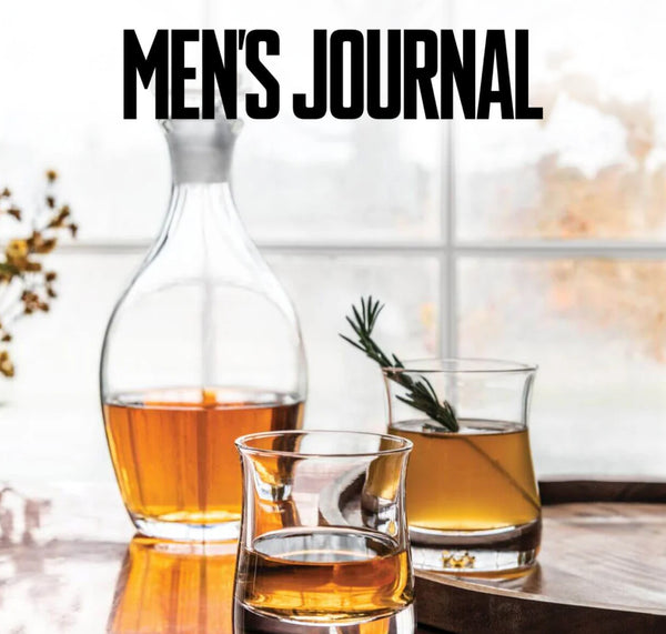 Men's Journal feature: Simon Pearce Woodbury Decanter filled with amber whiskey, alongside two handblown glass tumblers on a wooden tray