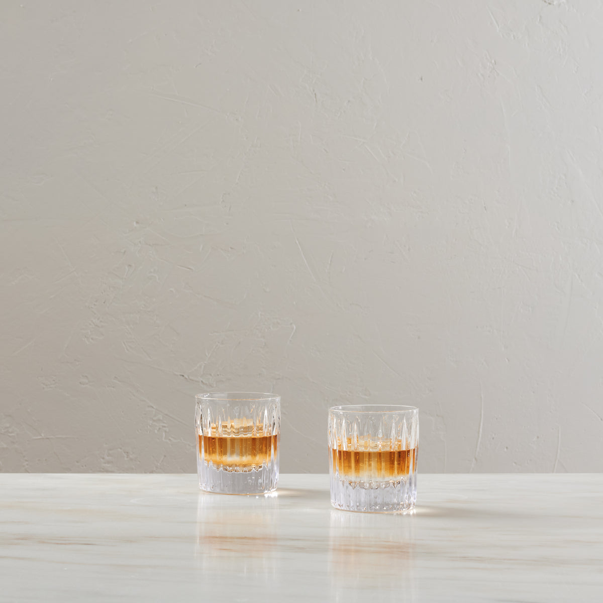 Two crystal double old-fashioned glasses with amber liquid and cut pattern design on white surface.