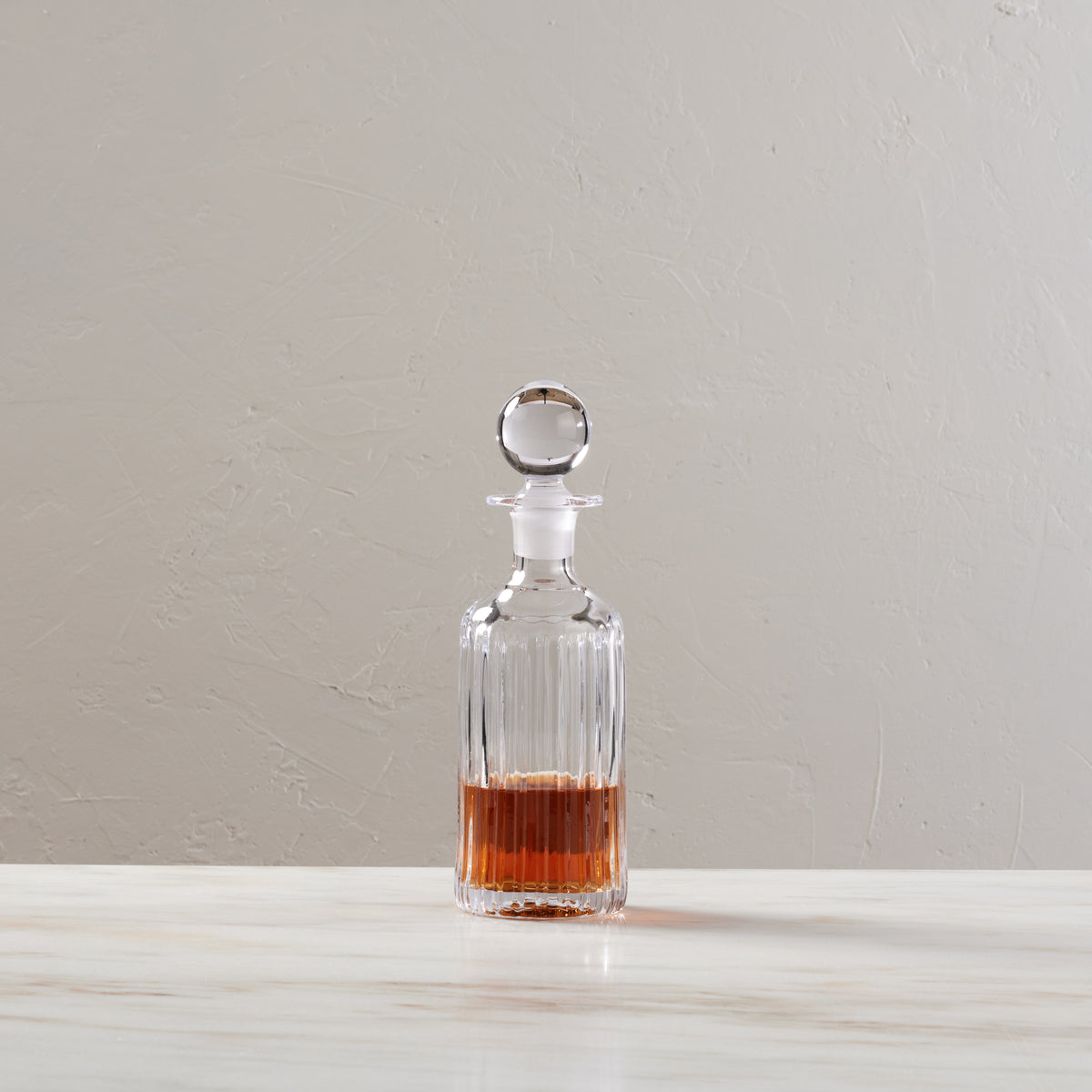 Clear glass decanter with vertical ribbed pattern, spherical stopper, filled with amber liquid.