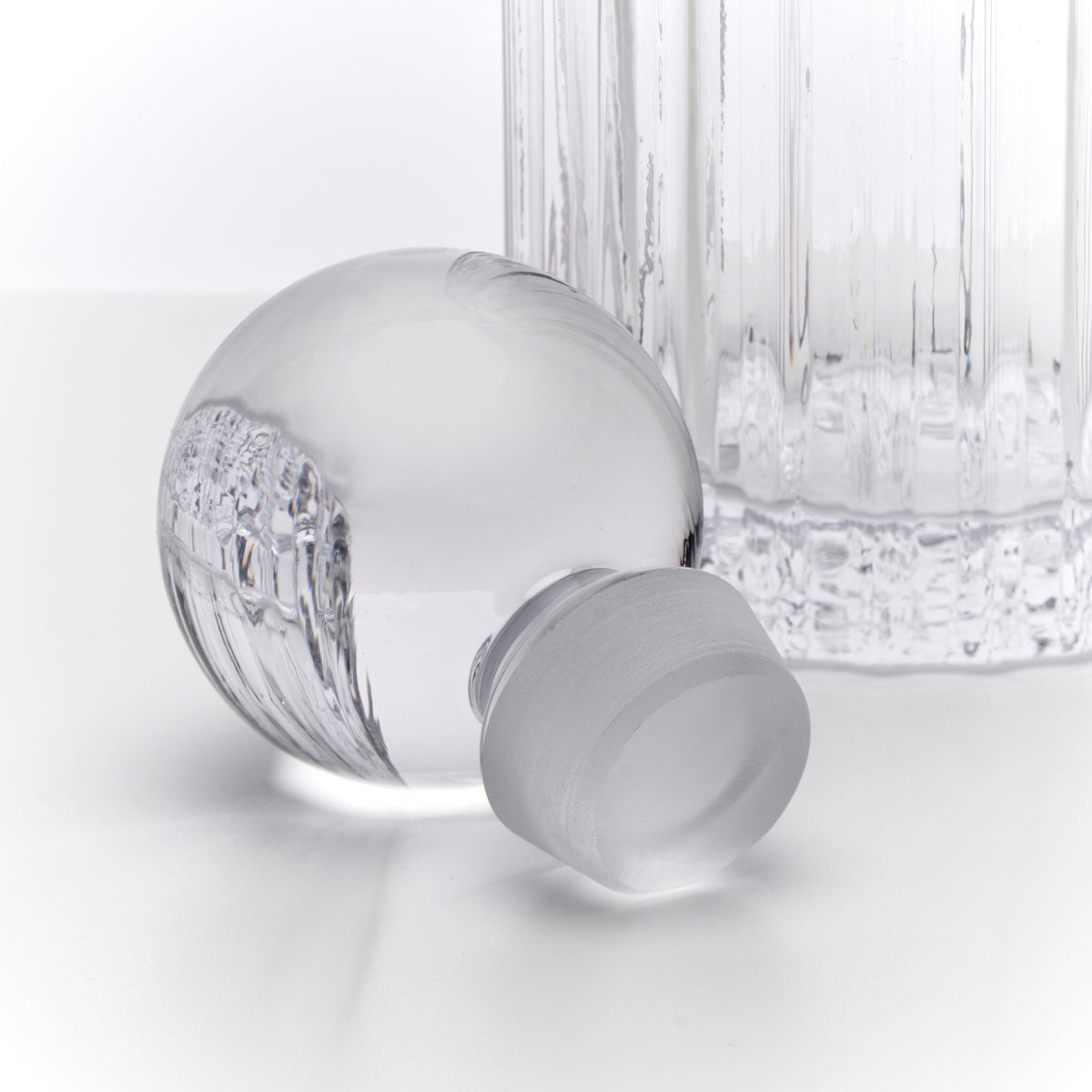 Crystal decanter with spherical body, textured lower section, matching stopper, and tall cylindrical glass beside it.