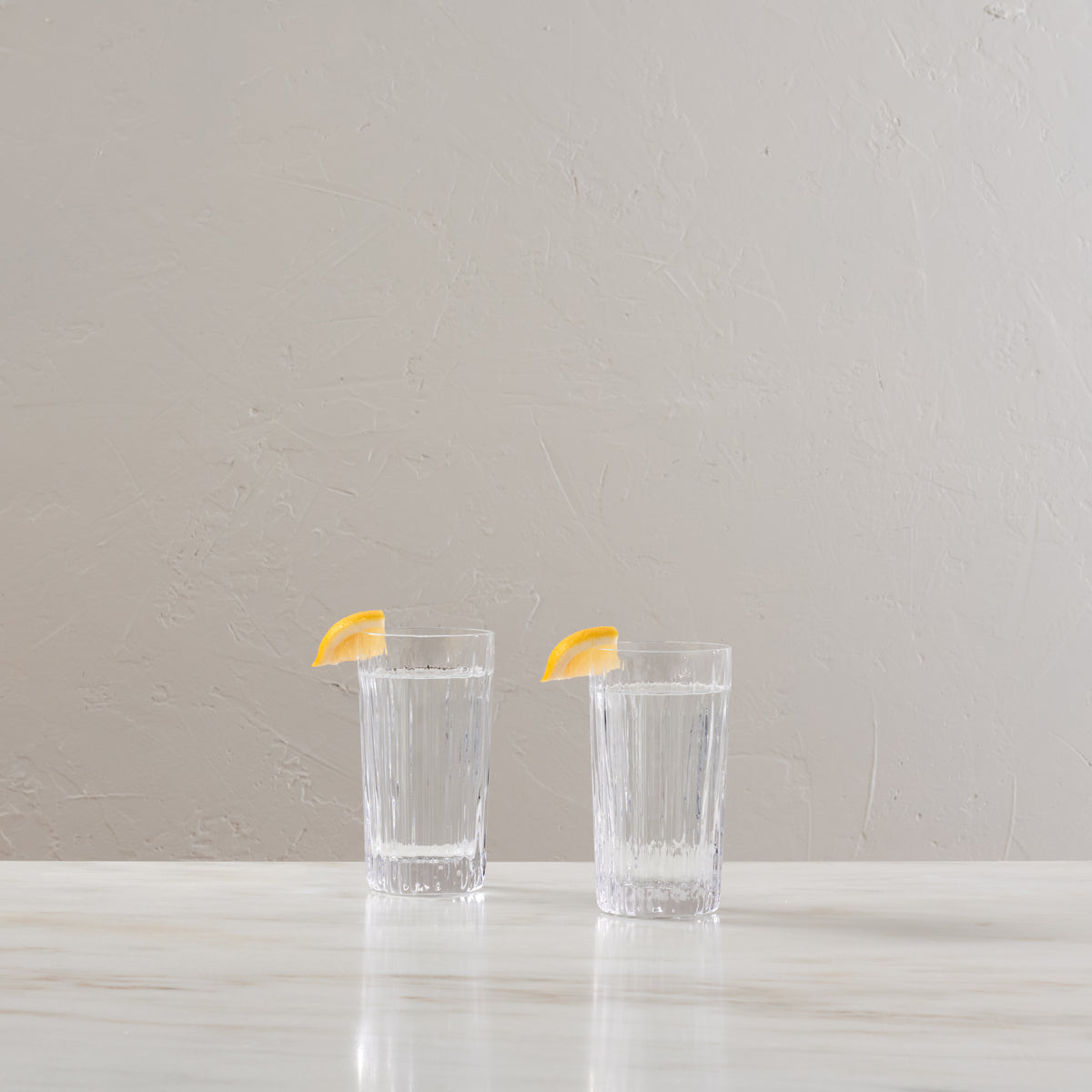 Two clear highball glasses with vertical ribbed texture, each garnished with a lemon slice.
