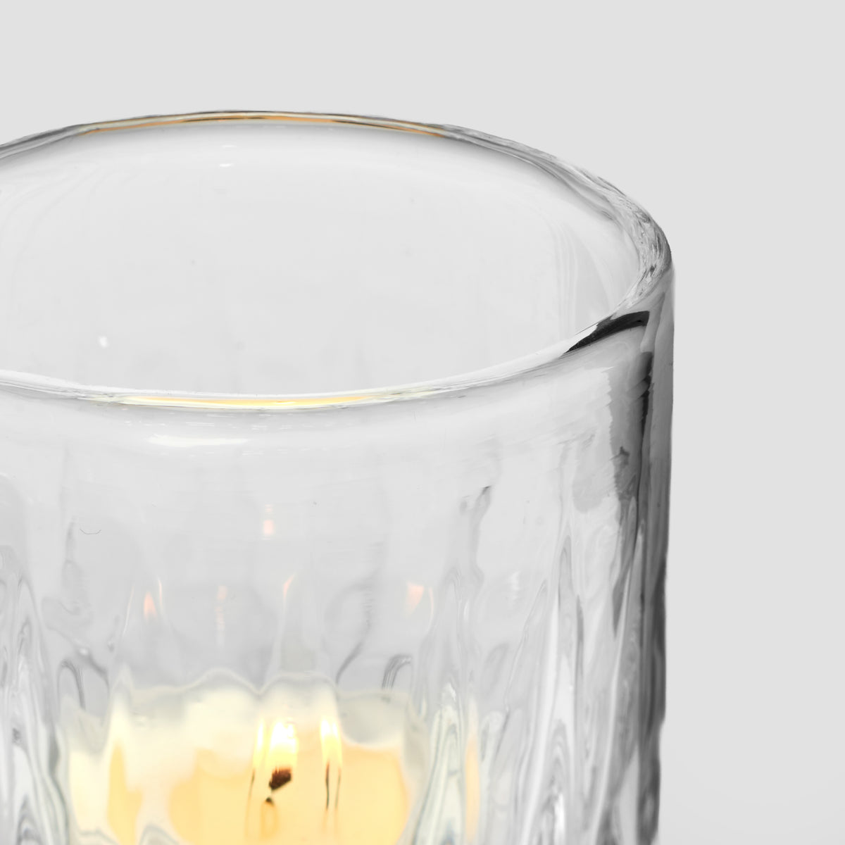 Clear glass tealight holder with gold rim and cream-colored wax candle inside.