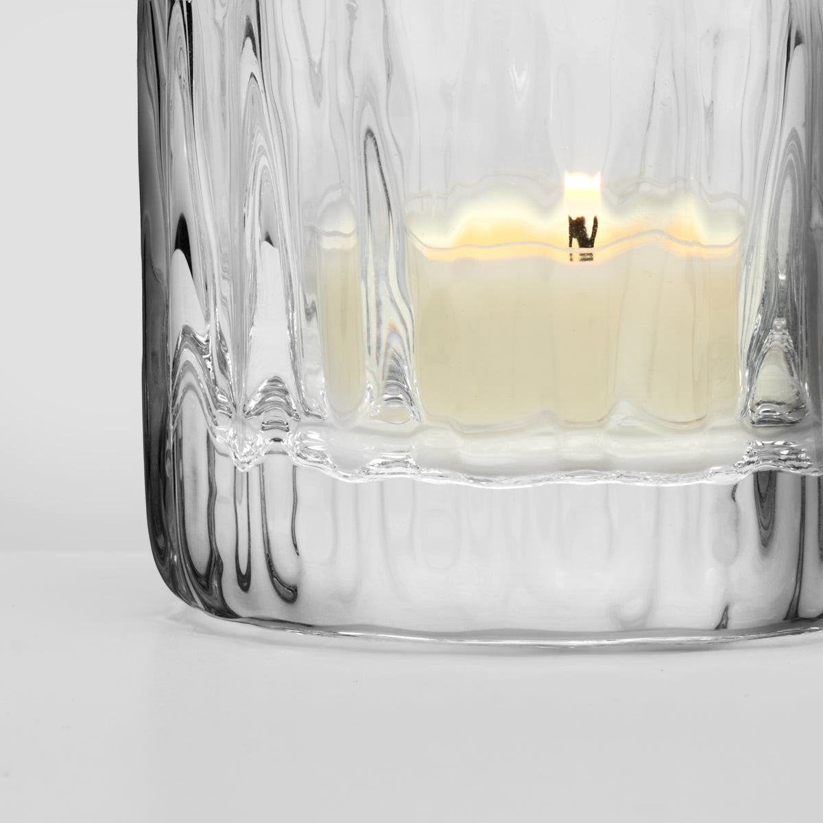 Clear glass container with textured ribbed sides holding a lit cream-colored tealight candle.