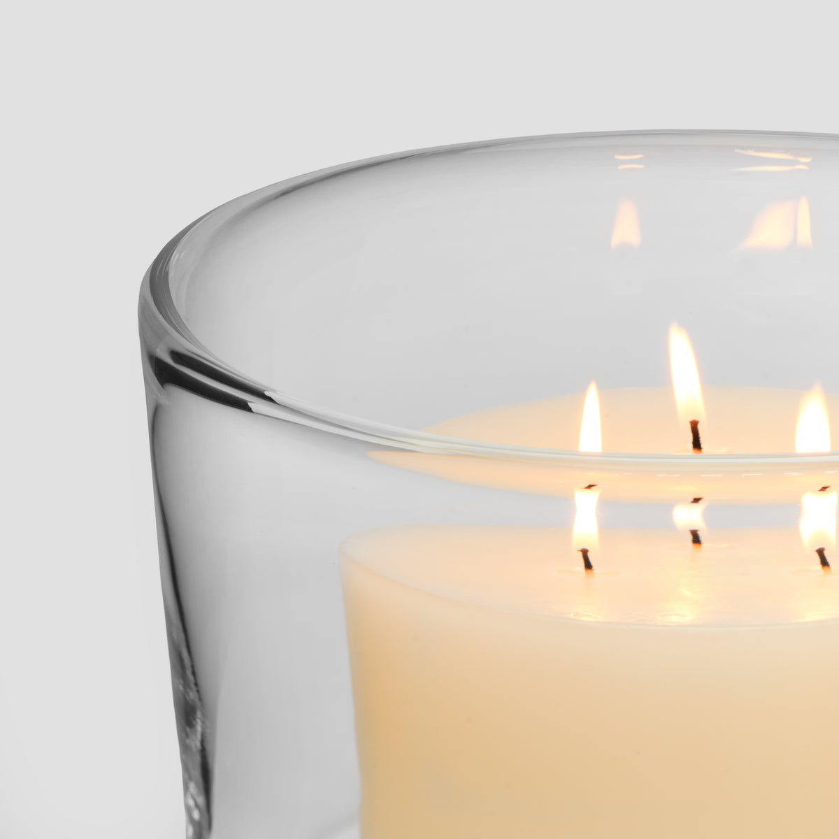 Clear glass hurricane with multiple lit cream-colored candles inside.