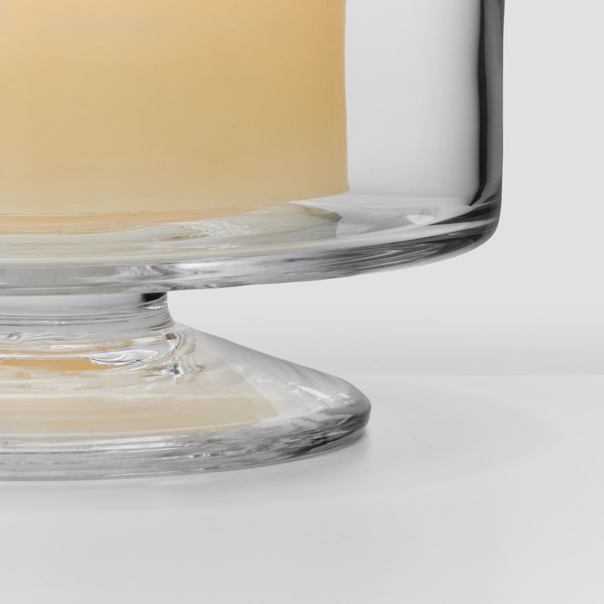 Clear glass hurricane with cream-colored cylindrical shade and wide circular base.