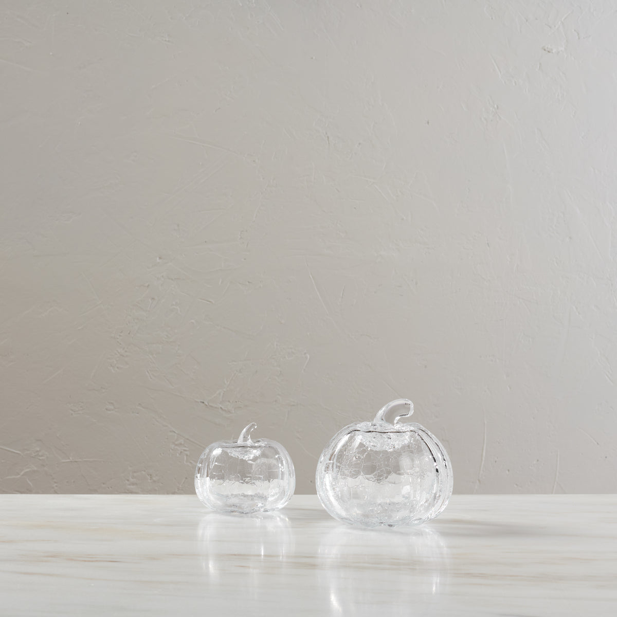 Two clear glass pumpkins with textured crackle finish and stems displayed on a white surface.
