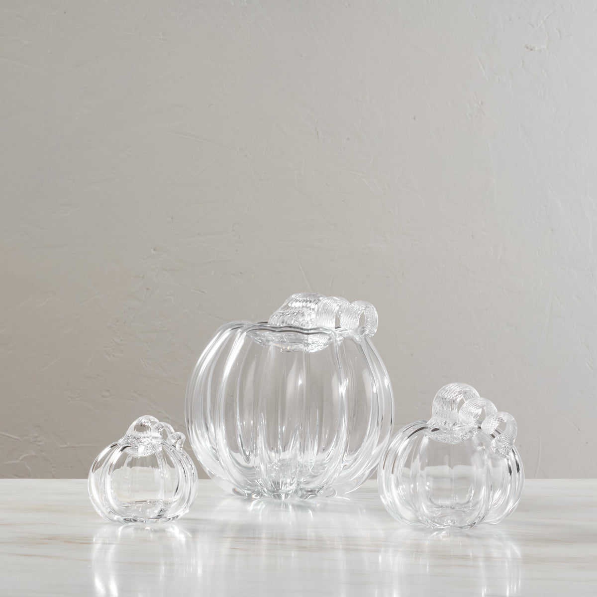 Three clear glass pumpkin-shaped containers with twisted stems, one large in center and two smaller flanking it.