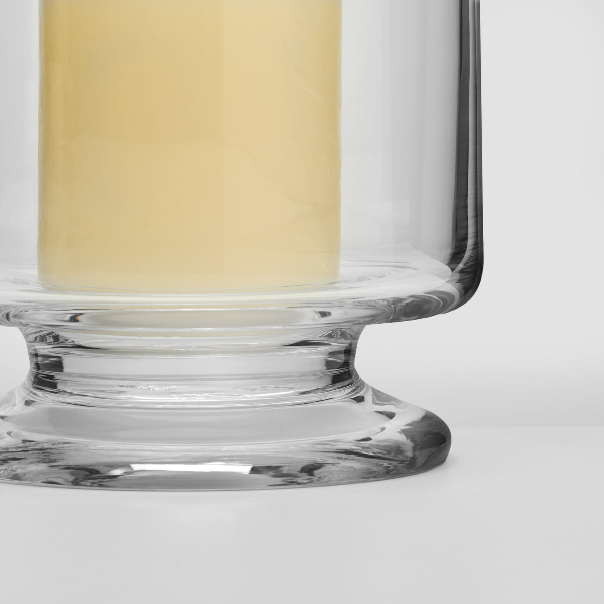 Glass hurricane candle holder with cream-colored candle and wide pedestal base.