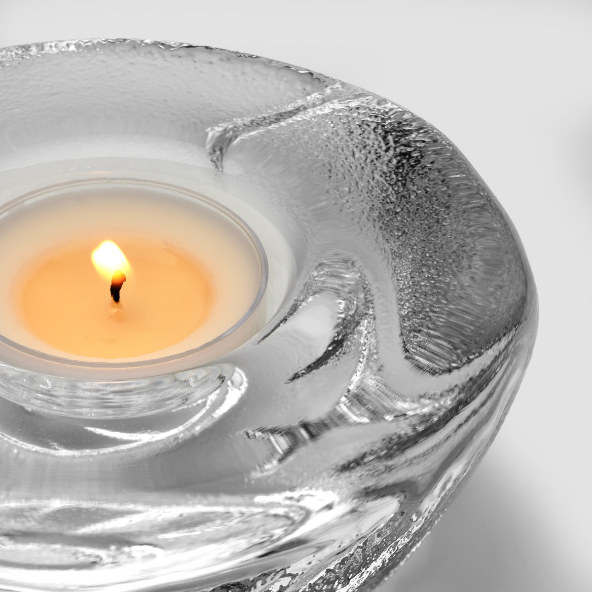 Lit cream tealight inside a silver shell-shaped glass holder with textured surface.