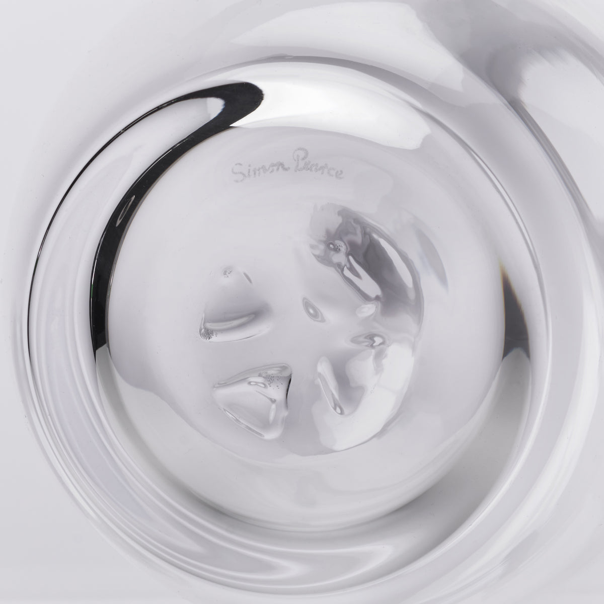 Clear glass decanter with black curved handle and etched designer signature on the body.