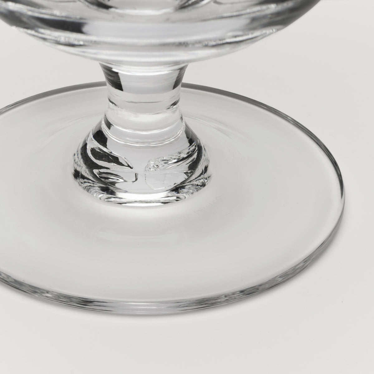 Close-up of a clear glass pedestal bowl or cup base on a light gray background.