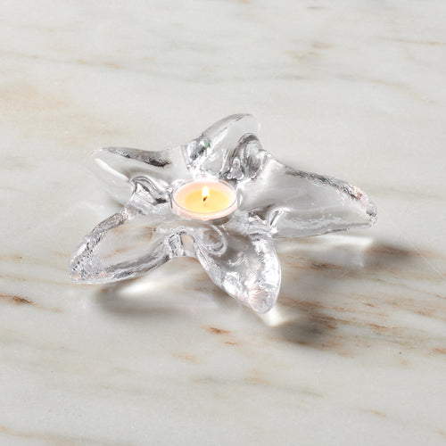 Clear glass starfish-shaped tealight holder with lit cream candle in center on marble surface.
