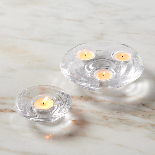 Clear glass tealight holders with one small and one larger trio holder, each containing lit cream-colored tealights on marble
