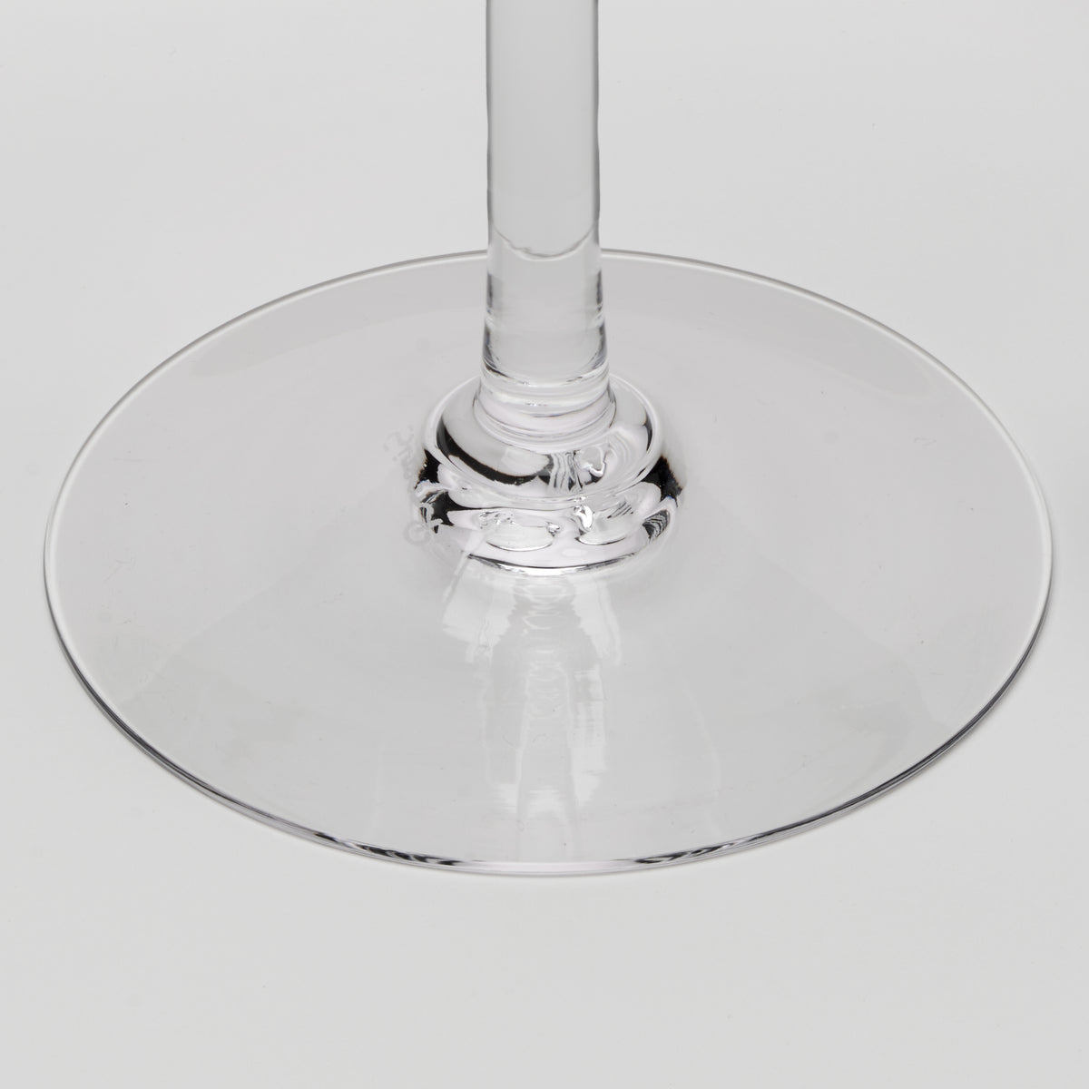 Close-up of a clear glass wine glass base and stem on a light gray background.