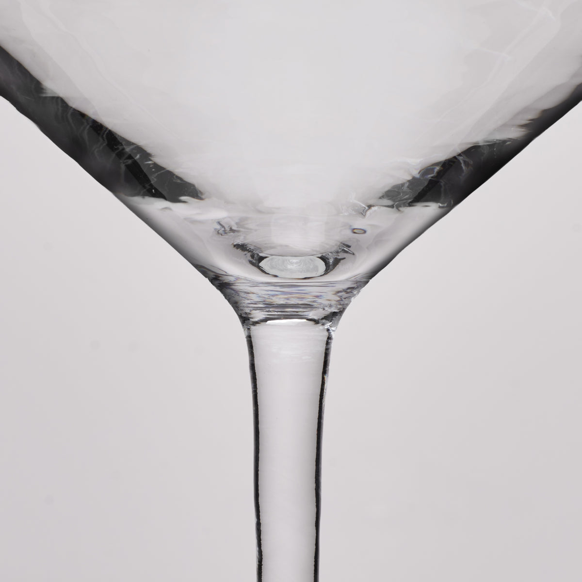 Close-up of a clear glass martini glass showing the base and stem against a light gray background.