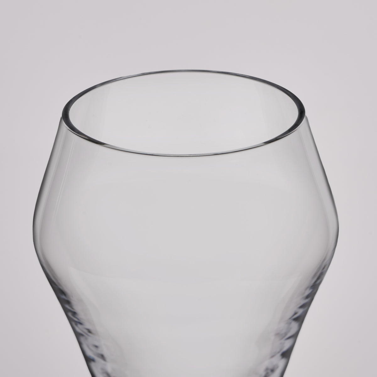 A close-up of a clear glass tumbler with a rounded, bulbous body and a textured base, shown against a neutral light gray background.