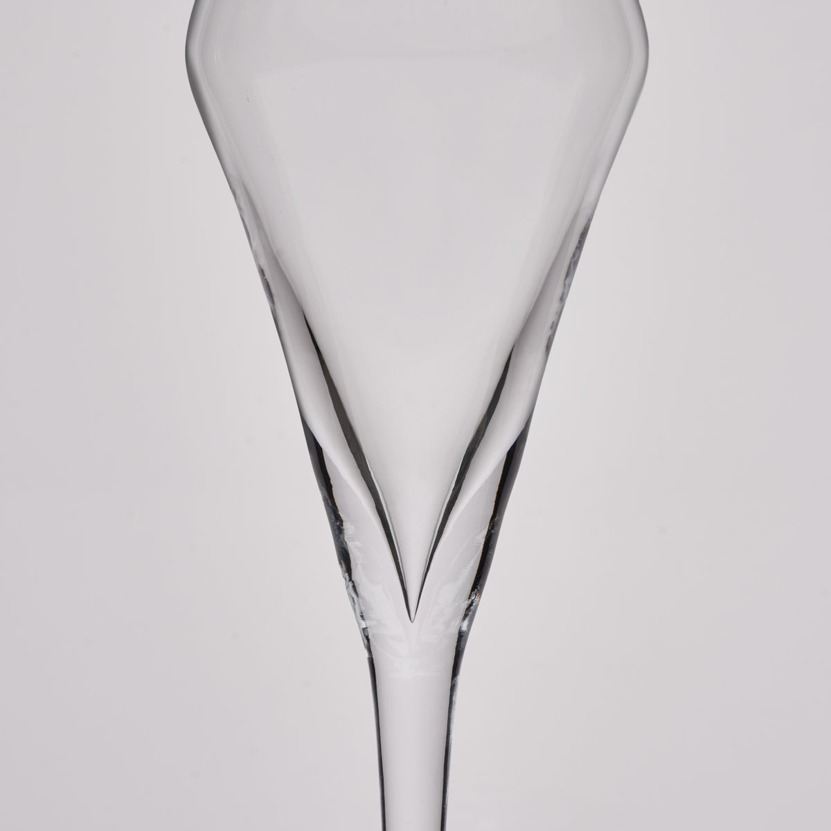 A clear glass champagne flute shown from the back against a light gray studio background.