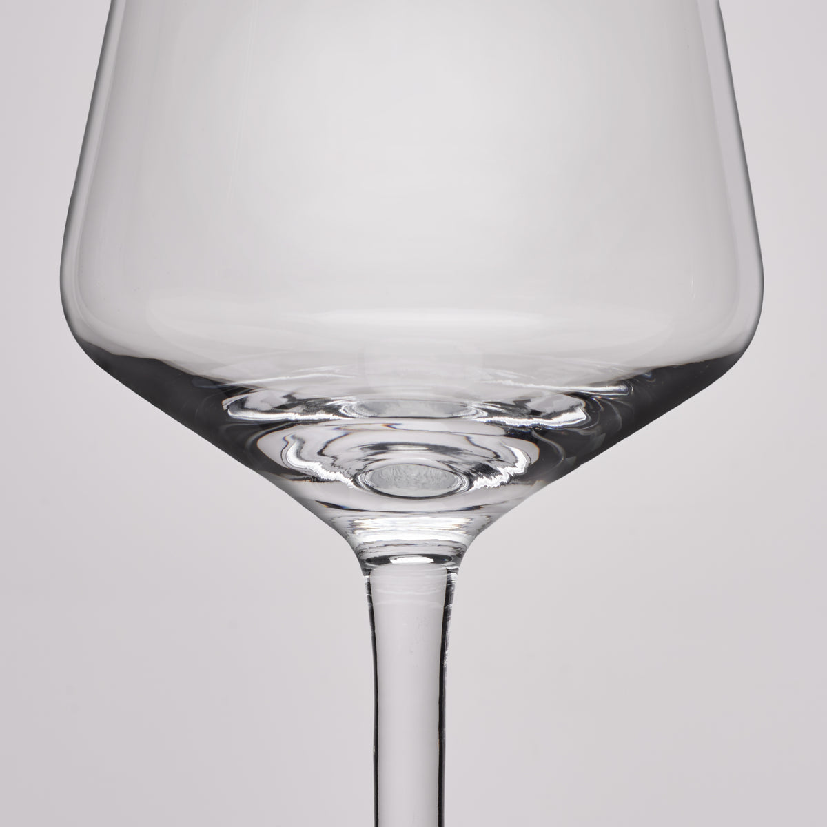A close-up studio shot of a clear glass wine glass against a light gray background.