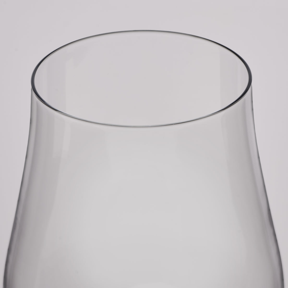 Close-up of a clear glass showing the top rim and flared glass body against a light gray background.