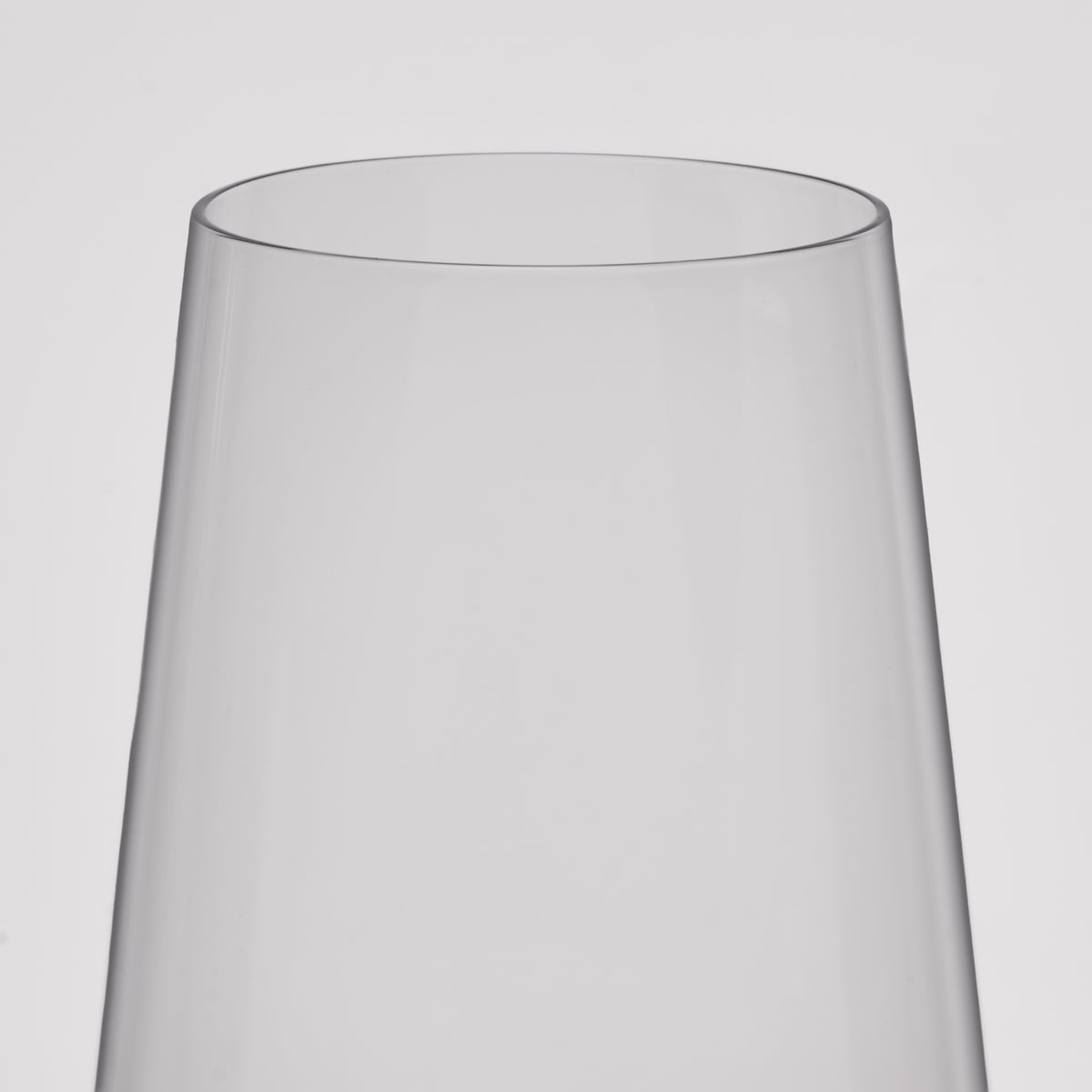 A close-up of a clear wine glass with a flared, tapered rim, shown against a plain light gray background.