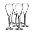 Six clear glass flutes with tapered bowls and solid bases arranged in a group.