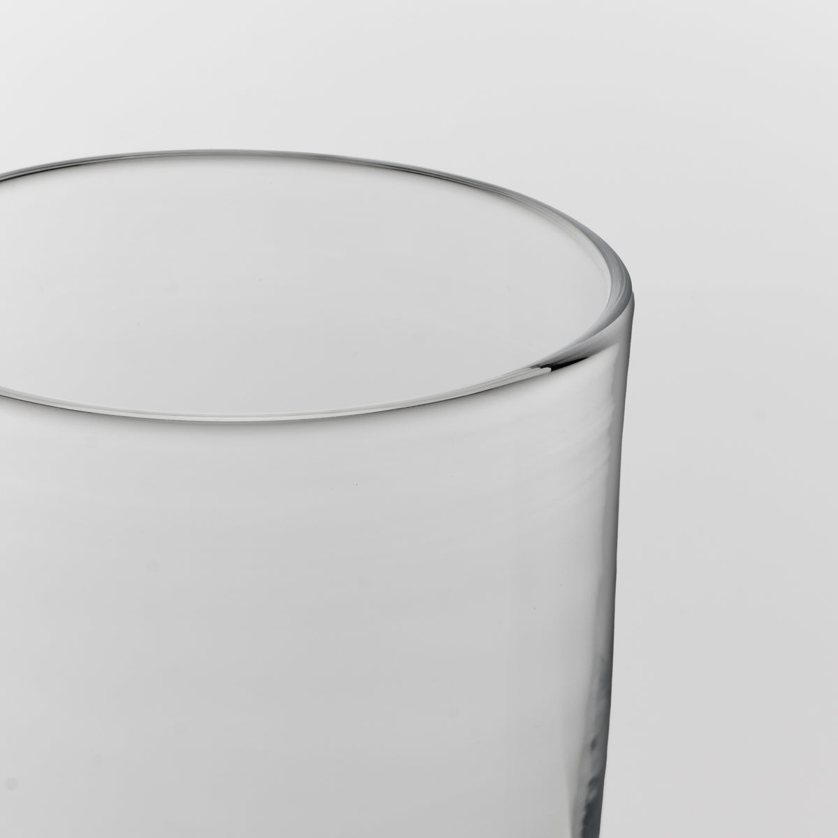 Close-up of a clear glass tumbler showing the rim and upper body against a light gray background.