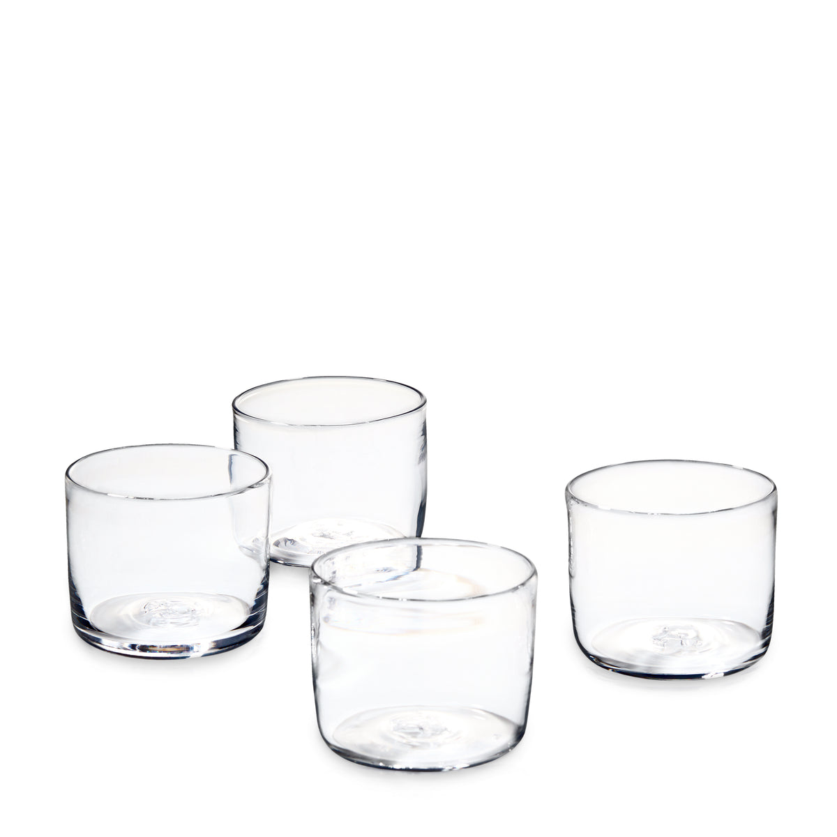 Four clear cylindrical drinking glasses with thick bases arranged in a group.
