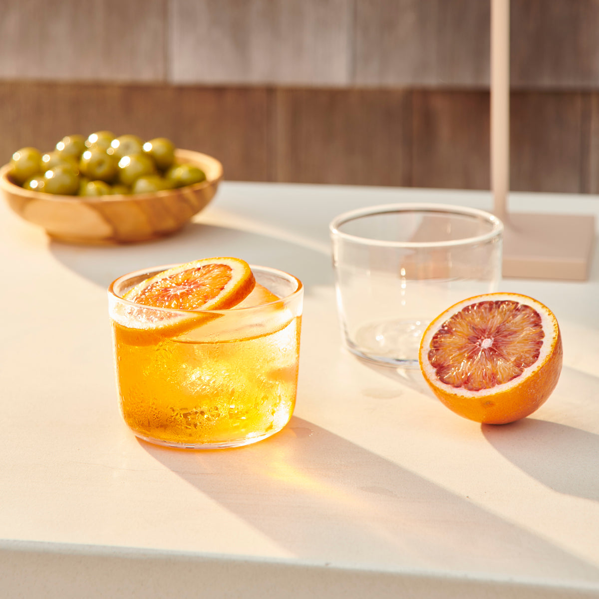Four clear glass cups displayed on a table with citrus fruits and beverages.
