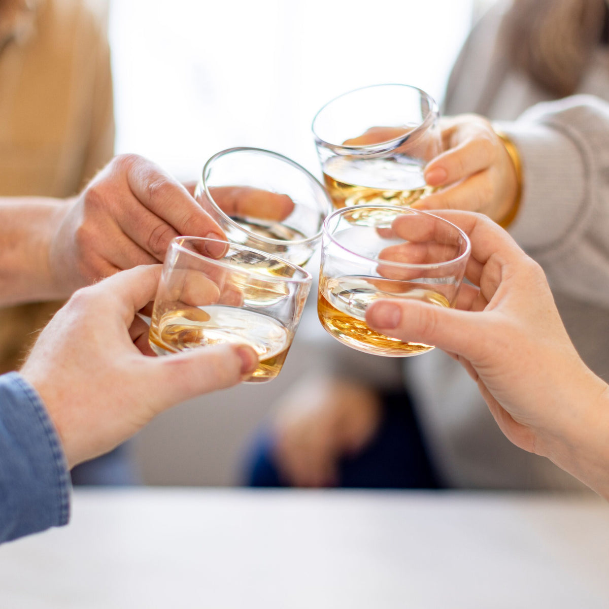 Four clear glass cups filled with amber liquid, held together in a toast by multiple hands.