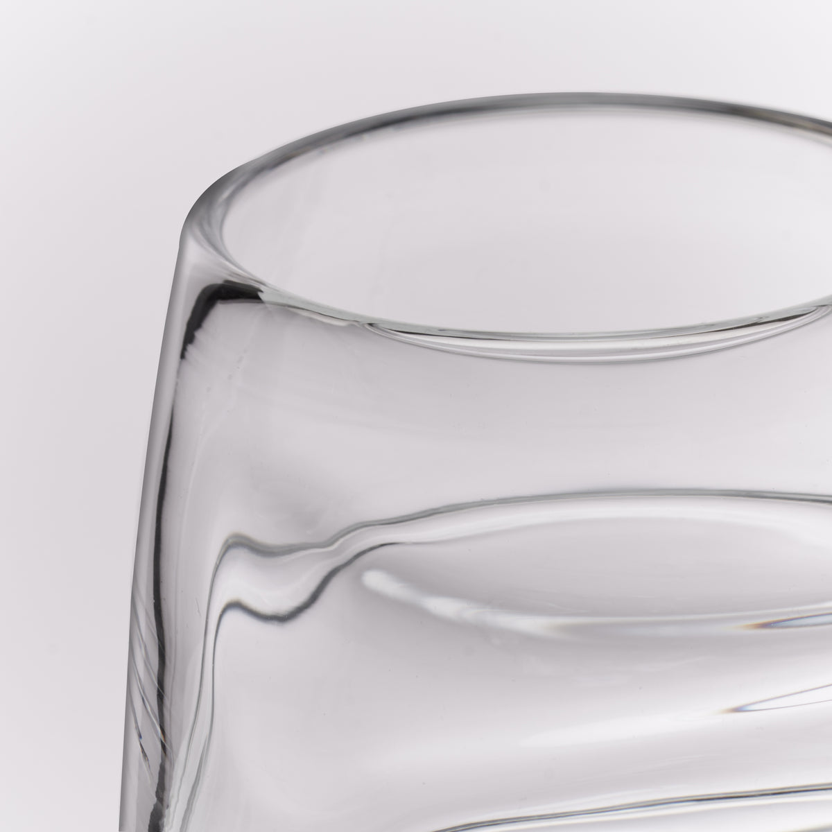 Close-up of a clear glass tumbler with a thick, rounded rim and smooth curved glass body on a light gray background.