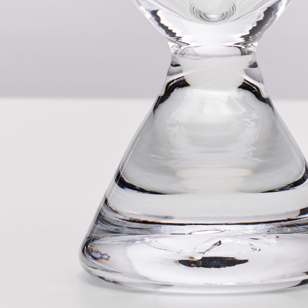 Clear glass stemless martini glass with wide bowl and narrow base, partially filled with liquid.