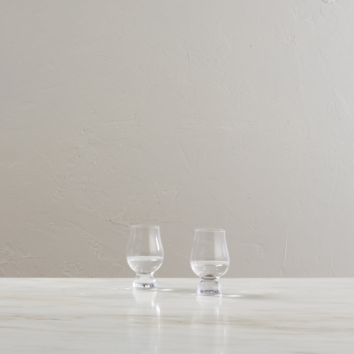Two clear glass tasting glasses with footed bases displayed on a white surface.