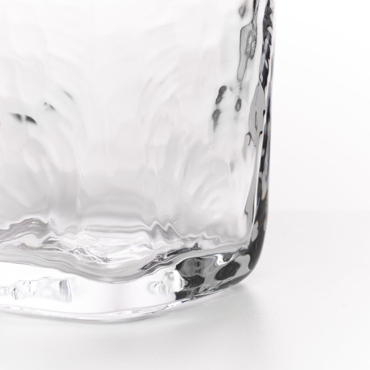 Close-up of a clear textured glass tumbler showing the corner and base detail against a white background.