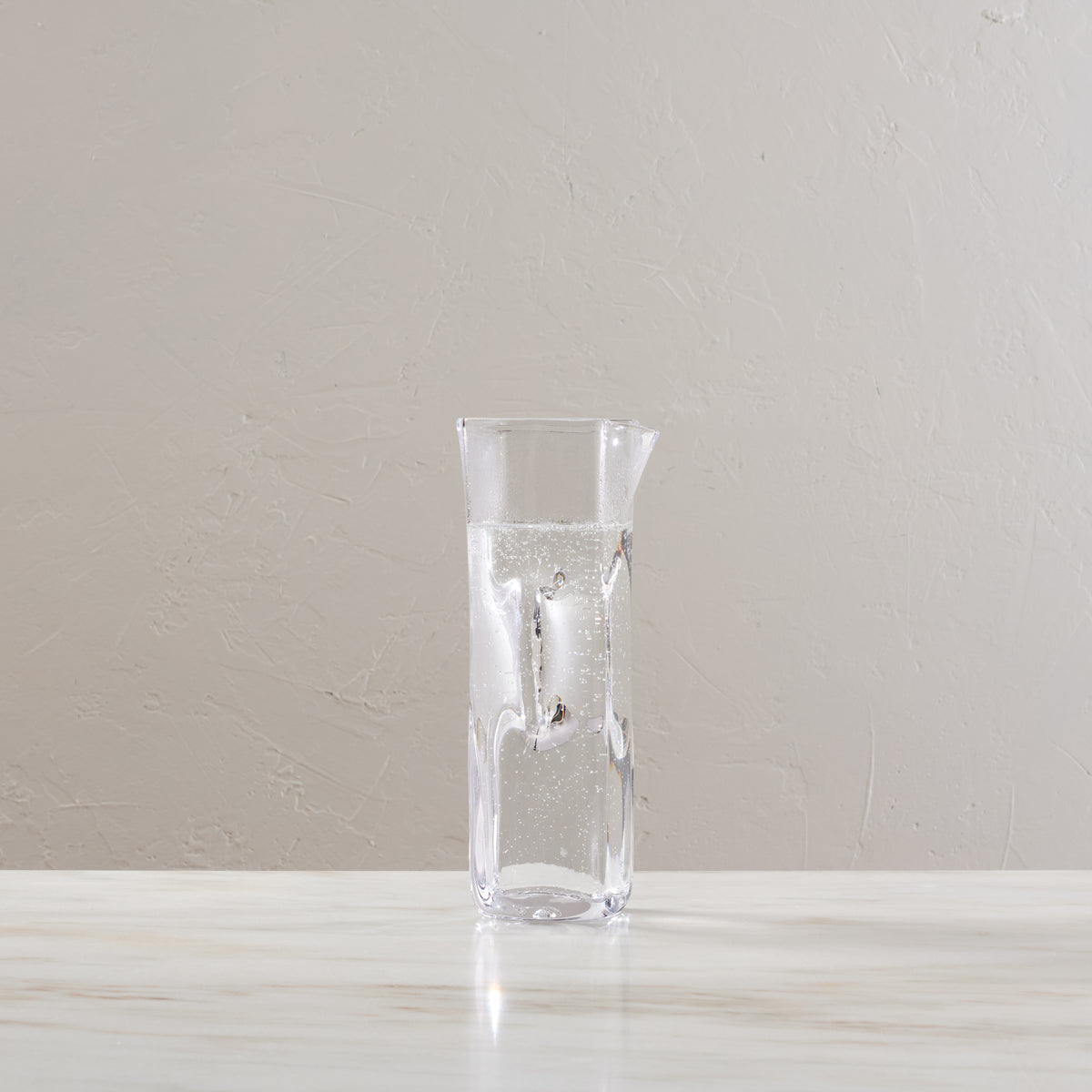 Clear glass carafe with tapered cylindrical shape, partially filled with carbonated water and ice cubes.
