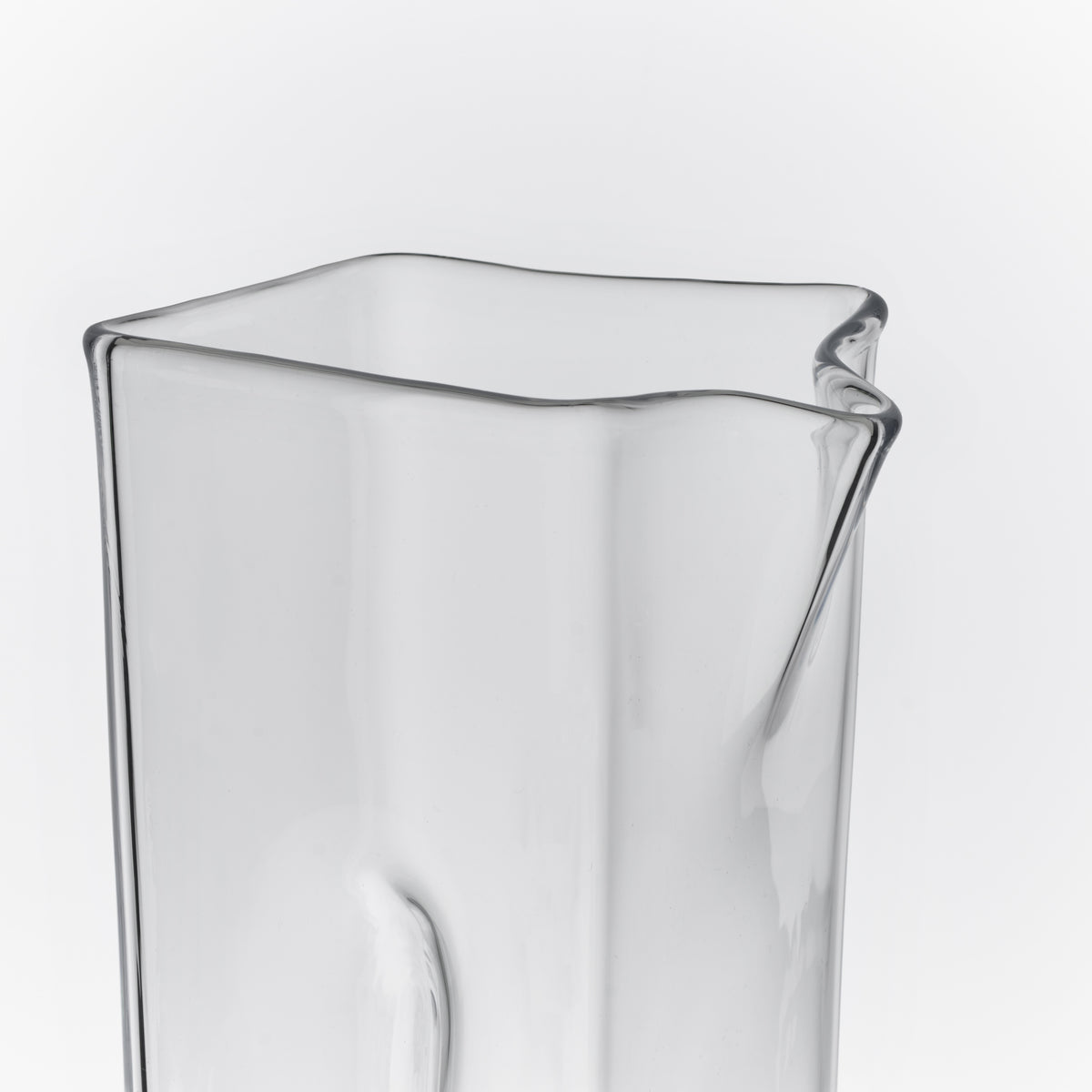 Clear glass carafe with curved wavy rim and pouring spout on one side.