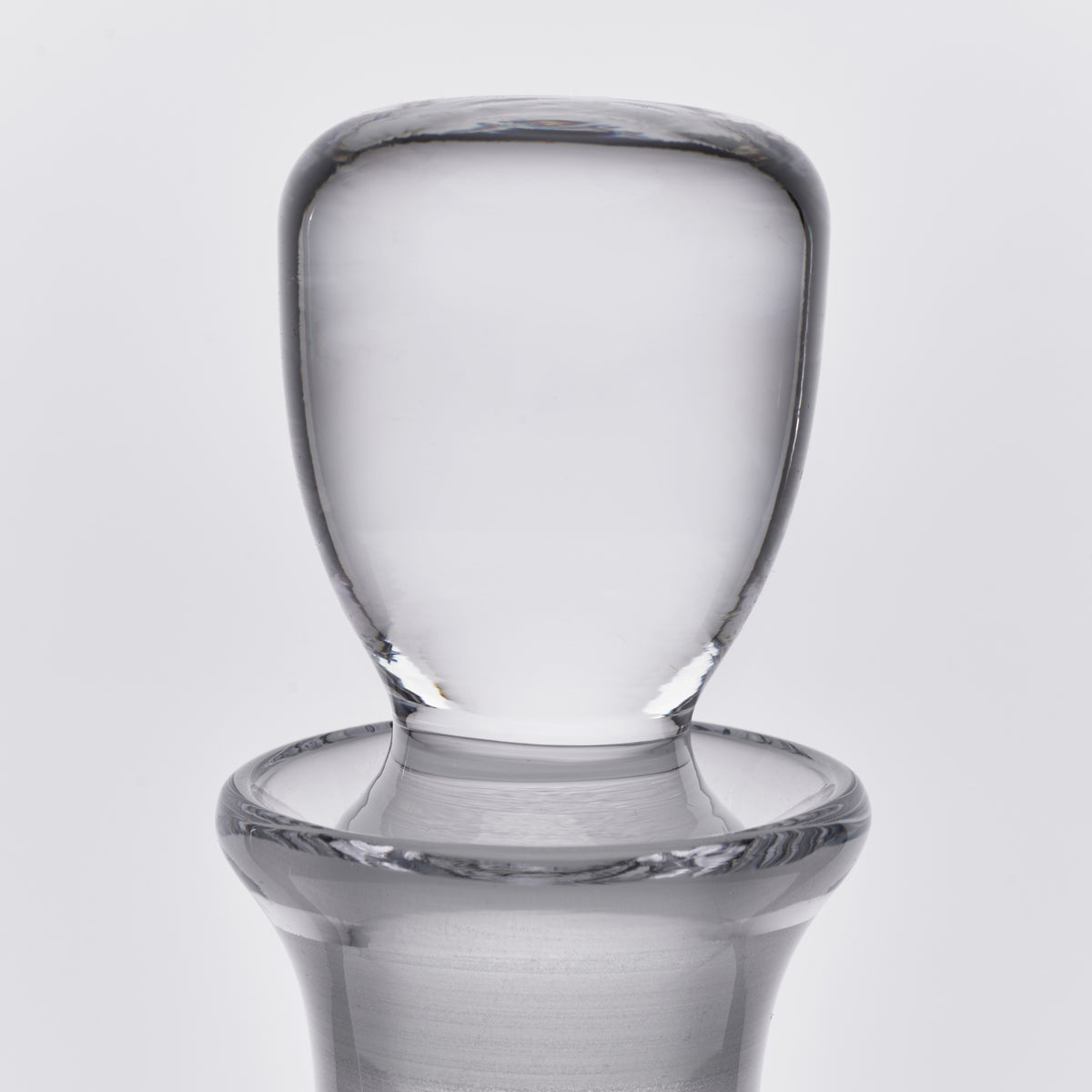 Clear glass decanter with rounded shoulders, cylindrical neck, and wide flat stopper on neutral background.