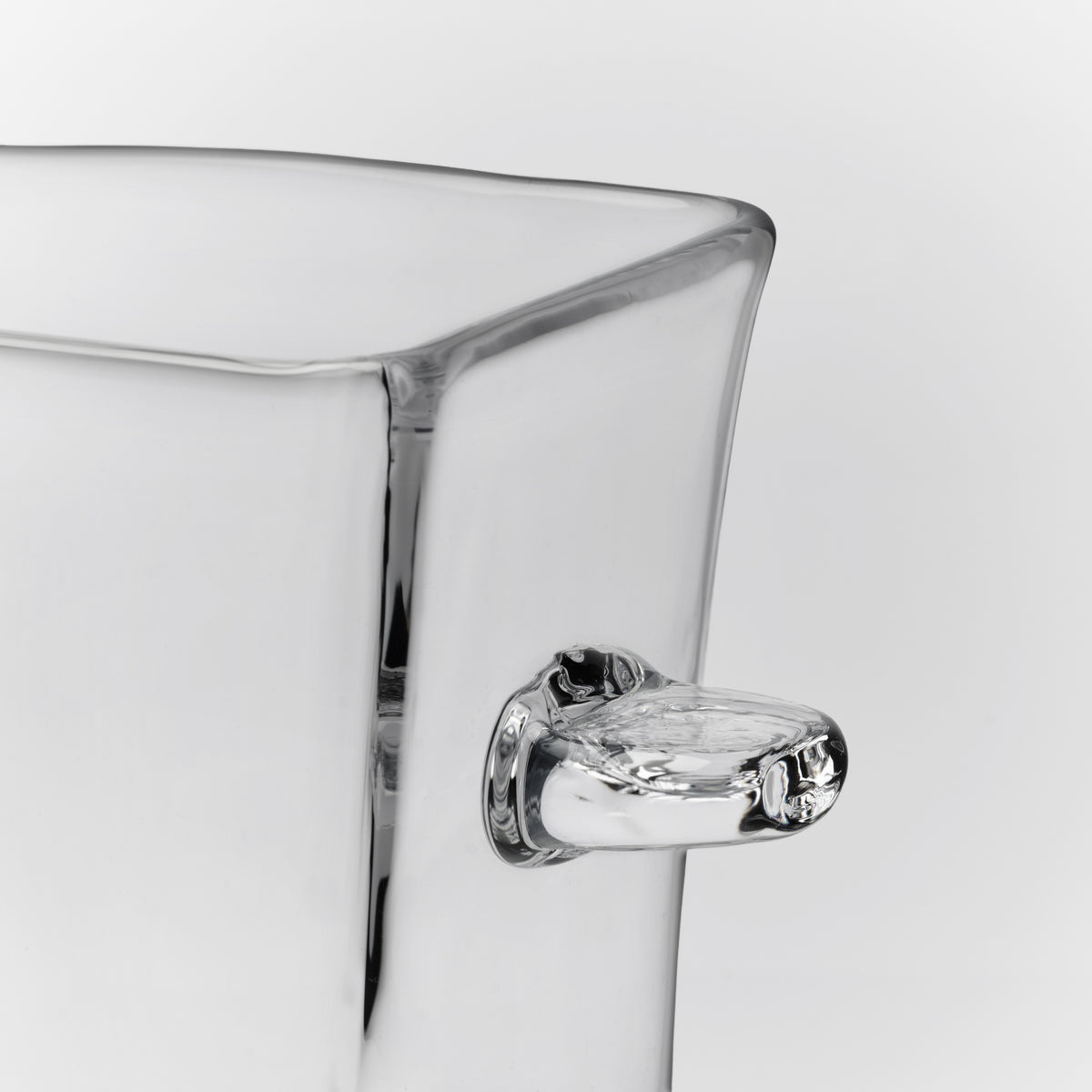 Clear glass ice bucket with curved rim and chrome-plated handle against white background.