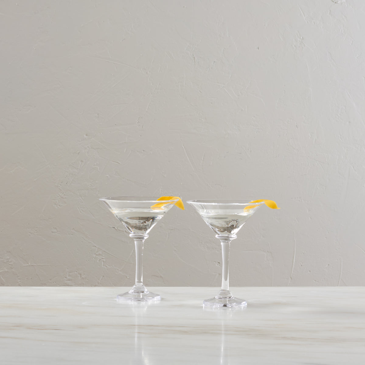 Two clear martini glasses filled with clear liquid and yellow lemon twists on rim.