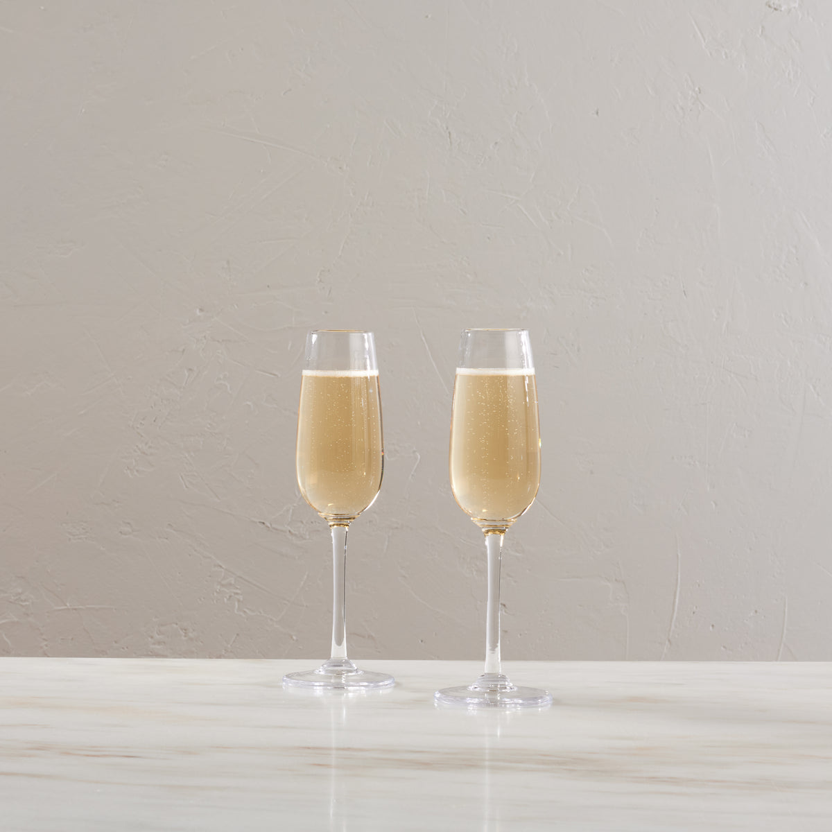 Two champagne flutes filled with sparkling wine on a white surface against a neutral background.