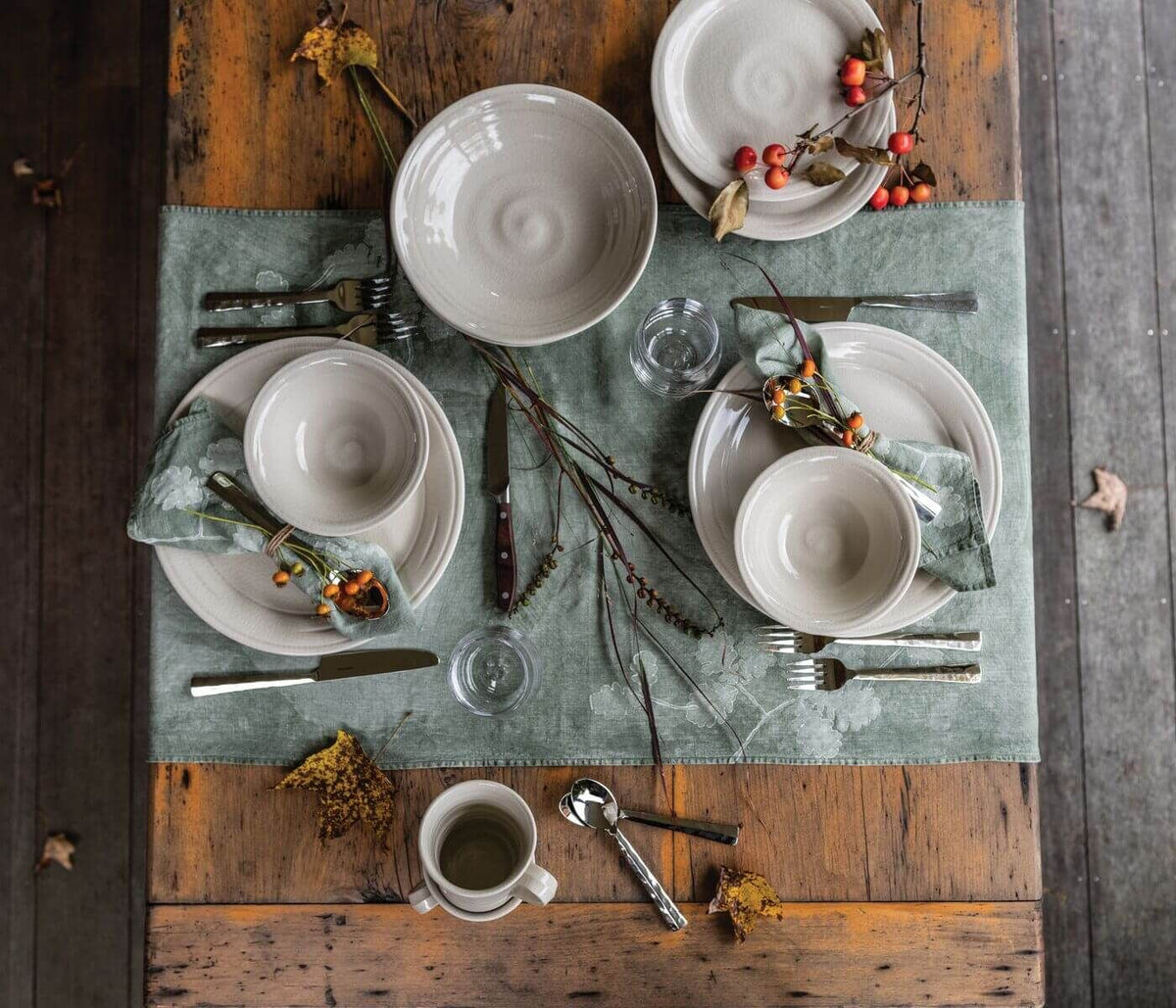 Ivory dinnerware set with crackle texture including bowls, plates, and cup arranged on table with utensils and dried flowers.