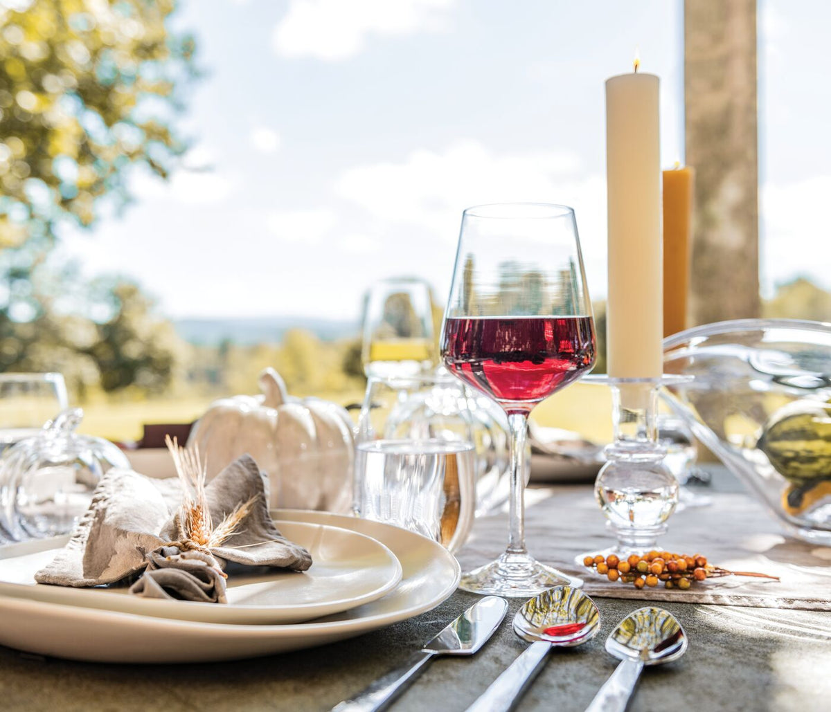 Cream-colored dinnerware plates stacked on outdoor table setting with wine glasses and candles.